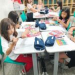 Crianças em suas mesas, uma de frente pra outra.